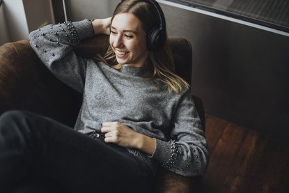 Frau mit Kopfhörer liegt auf dem Sofa.